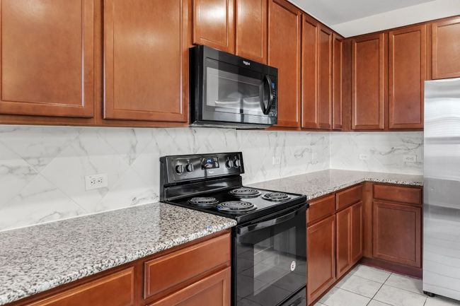 Kitchen with black appliances, light stone counters, decorative backsplash, and brown cabinets | Image 11