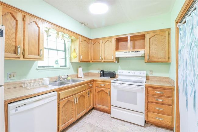 Kitchen featuring white appliances, under cabinet range hood, a sink, and light countertops | Image 6