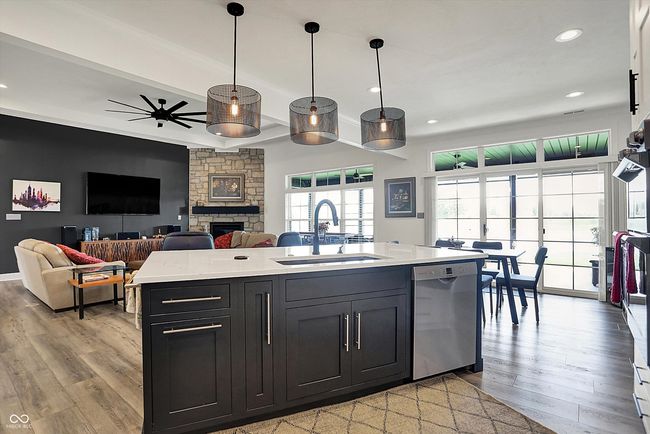 kitchen featuring light wood finished floors, a stone fireplace, stainless steel dishwasher, a sink, and ceiling fan | Image 12