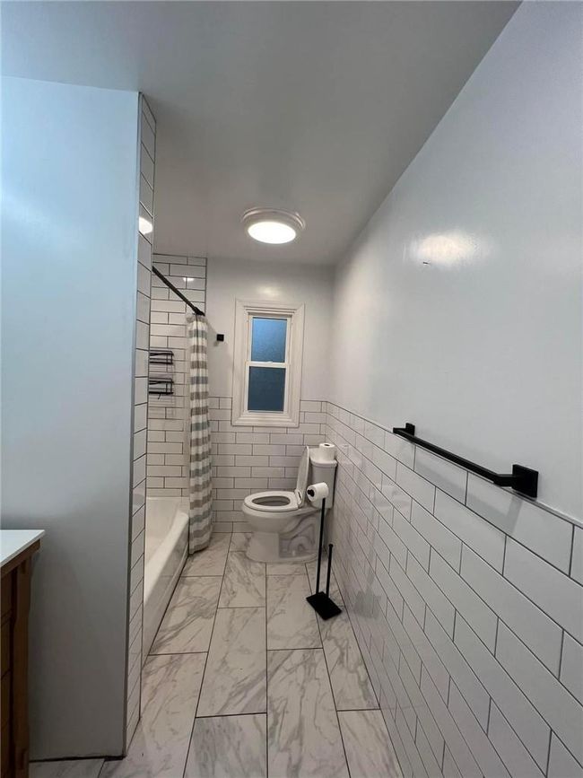 Bathroom with tile walls, a shower with curtain, toilet, and vanity | Image 8