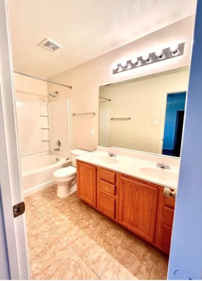 Bathroom featuring a textured ceiling, double vanity, toilet, tub / shower combination, and tile patterned floors | Image 14