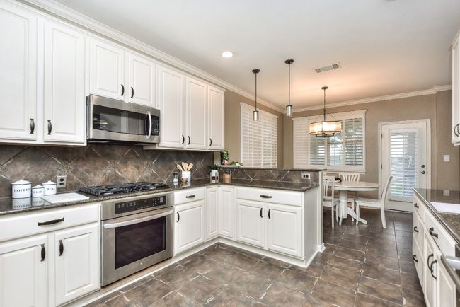 Charming kitchen features stainless appliances including gas cooktop, built-in oven and microwave, granite countertops, and pendant lighting. | Image 13