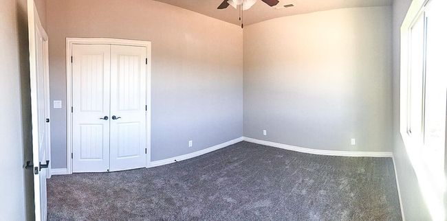 Spare room featuring vaulted ceiling, a ceiling fan, baseboards, dark colored carpet, and visible vents | Image 12