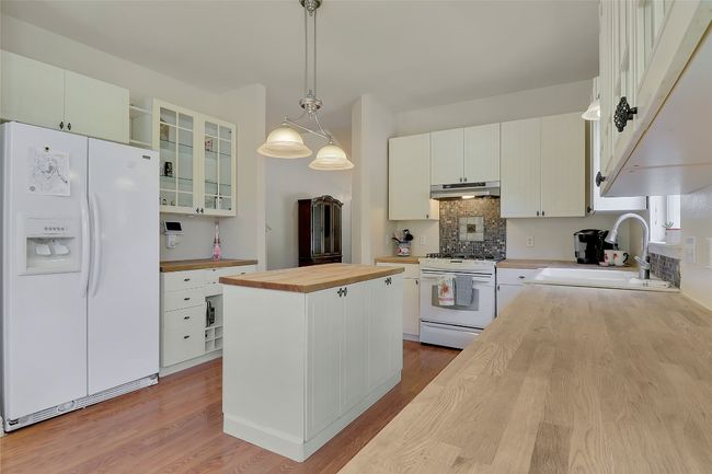Kitchen with butcher block countertops, white appliances, wood finished floors, and a center island | Image 10
