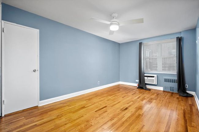 Spare room with radiator heating unit, wood finished floors, ceiling fan, and a wall unit AC | Image 15