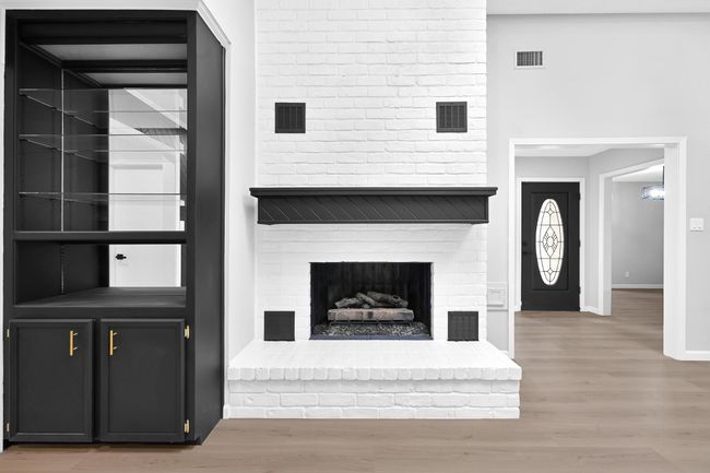 Striking white brick fireplace with a bold black mantel, serving as the focal point of the living room. The built-in black display cabinet with gold hardware adds a touch of elegance and functionality—perfect for showcasing décor or storing entertainment essentials. | Image 9