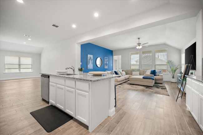 Kitchen with open floor plan, stainless steel dishwasher, light wood-type flooring, lofted ceiling, and white cabinetry | Image 7
