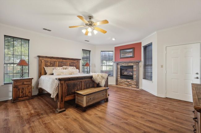 Primary Bedroom with wood finished floors, crown molding, a stone fireplace, multiple windows, and a ceiling fan | Image 20