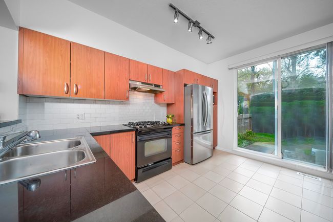 Kitchen featuring a sink, dark countertops, freestanding refrigerator, black gas stove, and under cabinet range hood | Image 20