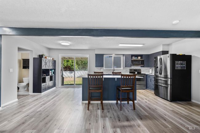 Kitchen with appliances with stainless steel finishes, light wood-style flooring, a kitchen breakfast bar, backsplash, and open shelves | Image 7