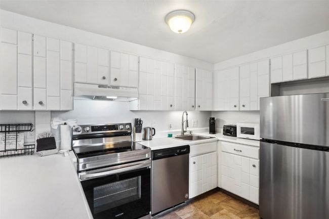 Kitchen with light countertops, under cabinet range hood, stainless steel appliances, and a sink | Image 13