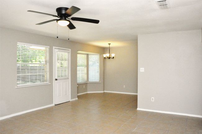 Looking at the dining area from living room with light tile patterned floors, visible vents, baseboards, and ceiling fan with notable chandelier | Image 9