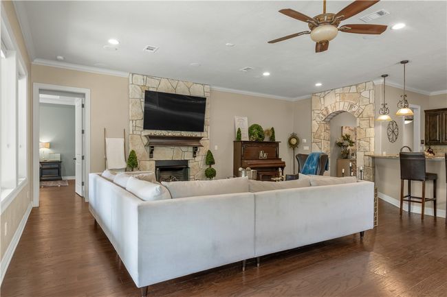 Living room featuring a ceiling fan, a stone fireplace, dark wood finished floors, crown molding, and baseboards | Image 11
