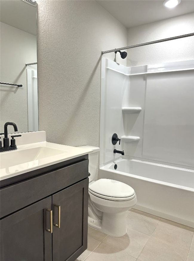 En-suite bath with vanity, shower combination, tile floors, toilet, and a textured wall | Image 16