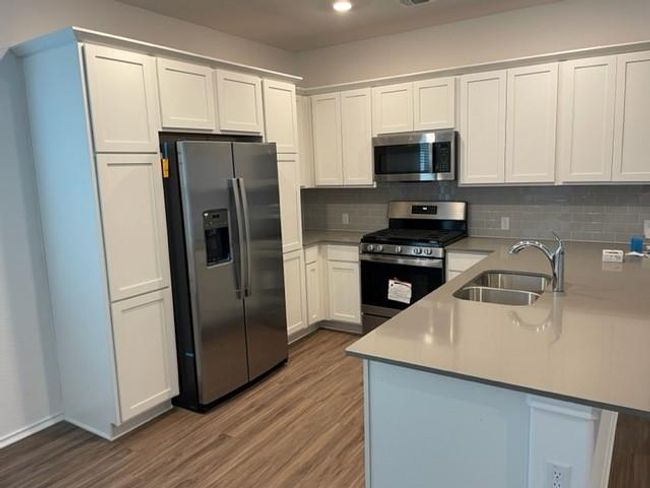 Kitchen with appliances with stainless steel finishes, a sink, a peninsula, wood finished floors, and backsplash | Image 6