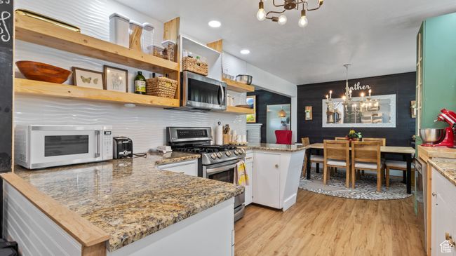 Kitchen with a peninsula, light wood-style floors, a chandelier, open shelves, and appliances with stainless steel finishes | Image 9