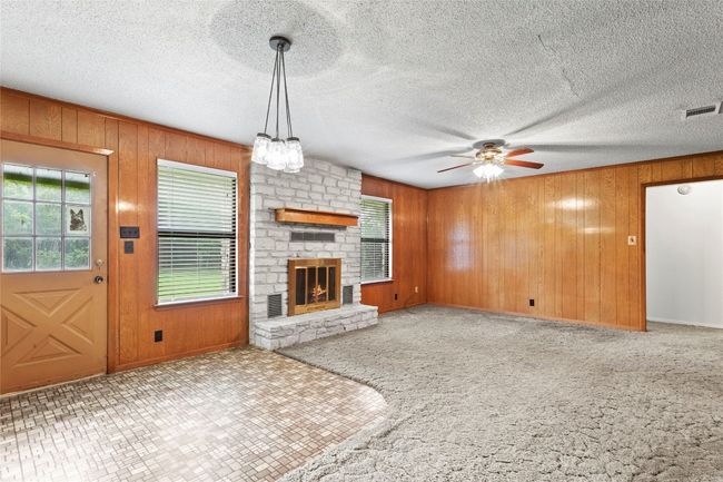 Unfurnished living room with plenty of natural light, a ceiling fan, wood walls, a large fireplace, and a textured ceiling | Image 13