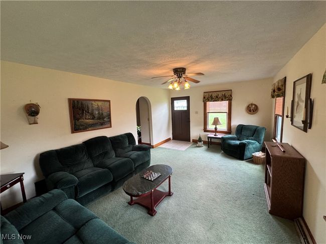 Carpeted living room featuring arched walkways, a ceiling fan, a textured ceiling, and baseboards | Image 24