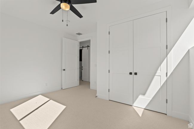 Unfurnished bedroom featuring a barn door, carpet, a ceiling fan, and a closet | Image 37