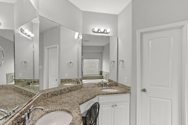 This Primary bathroom is complete with large mirrors, a vanity area, double sinks, granite countertops and backsplash. | Image 13