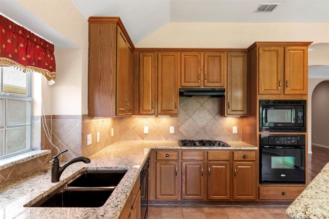 Kitchen with black appliances, a sink, brown cabinets, light stone countertops, and backsplash | Image 29