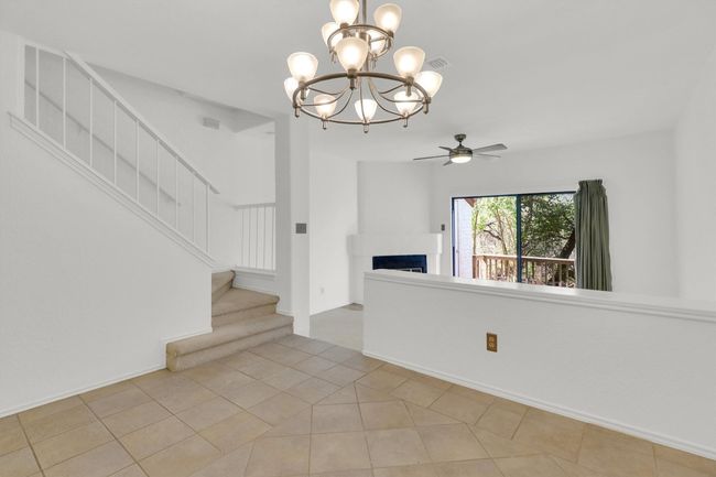 Spare room with stairs, a fireplace, ceiling fan with notable chandelier, light tile patterned floors, and baseboards | Image 11
