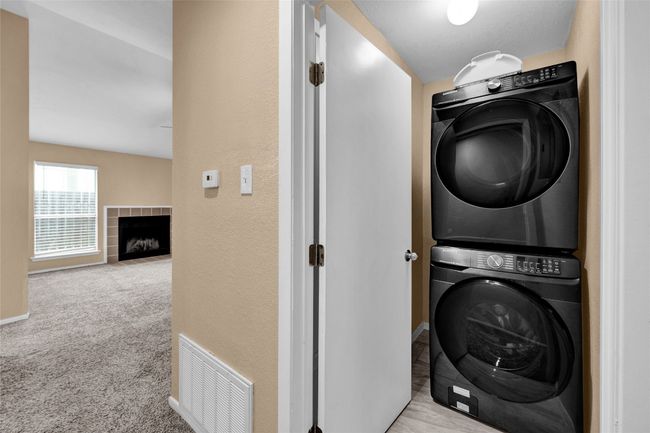 Laundry area with carpet flooring, visible vents, a tile fireplace, baseboards, and stacked washing maching and dryer | Image 13