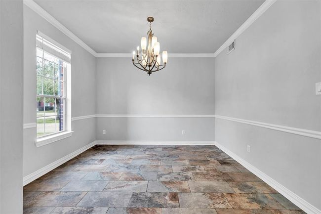 Bright dining room with a large window, elegant chandelier, and stylish tile flooring. The space features neutral gray walls with white trim and crown molding. | Image 6