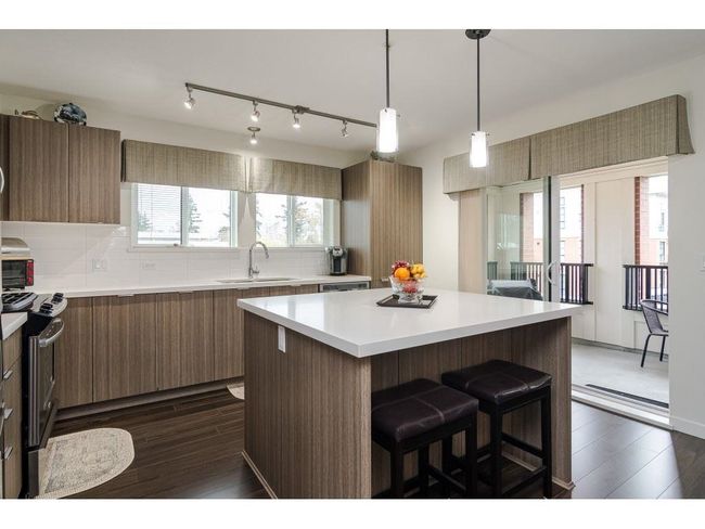 Kitchen featuring dark wood-style floors, a breakfast bar, light countertops, a sink, and stainless steel electric range | Image 6