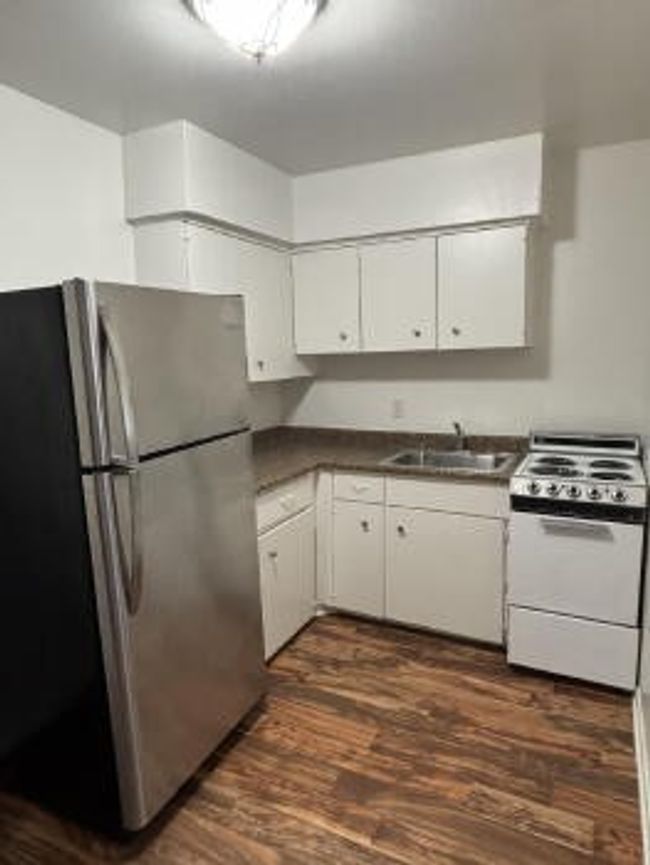 Kitchen with a sink, freestanding refrigerator, dark wood-style flooring, white electric stove, and dark countertops | Image 4