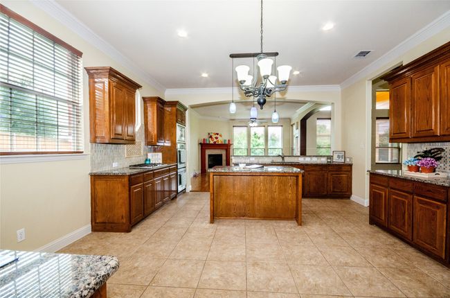 Kitchen with a chandelier, backsplash, stone counters, ornamental molding, and decorative light fixtures | Image 4