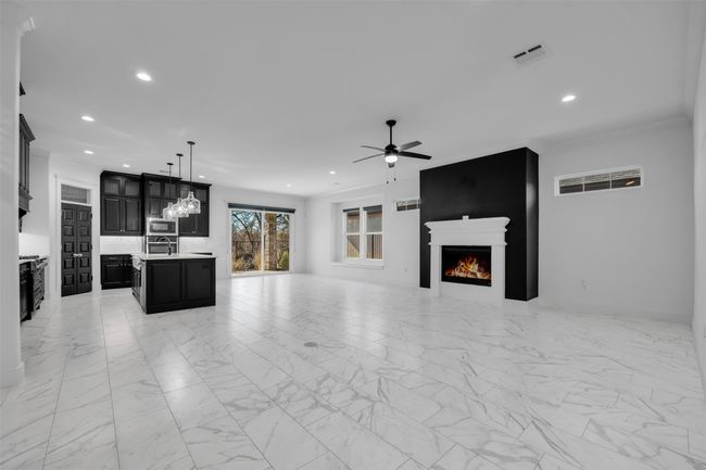 Unfurnished living room with a warm lit fireplace, visible vents, ceiling fan, and recessed lighting | Image 4