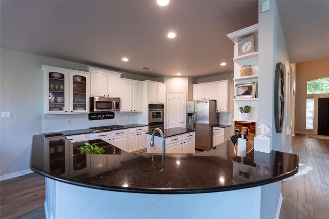 Kitchen featuring appliances with stainless steel finishes, open shelves, a large island with sink, dark wood finished floors, and recessed lighting | Image 15