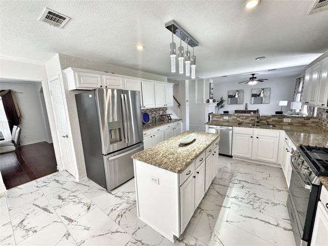 Kitchen with stainless steel appliances, a ceiling fan, white cabinetry, dark stone counters, and a peninsula | Image 9