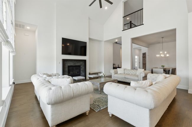 Living room featuring a glass covered fireplace, high vaulted ceiling, ceiling fan, a chandelier, and dark wood-style floors | Image 7