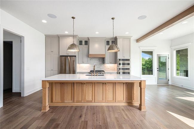 Kitchen with stainless steel appliances, wood finished floors, backsplash, light countertops, and a large island with sink | Image 22