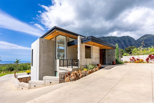 View of the front of the home, down a long private driveway, multiple tandem stalls on the right, and the driveway continues to the back of the house which hosts a carport. Elevator shaft visible on the left (concrete exterior). | Image 23