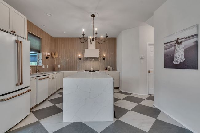 Kitchen with white appliances, a sink, a center island, a chandelier, and white cabinets | Image 14