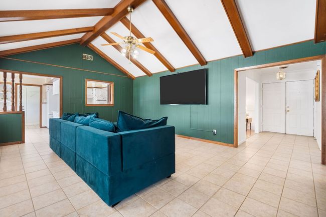 Living room featuring ceiling fan, original wood beams, light tile patterned floors, and wood panel walls | Image 13