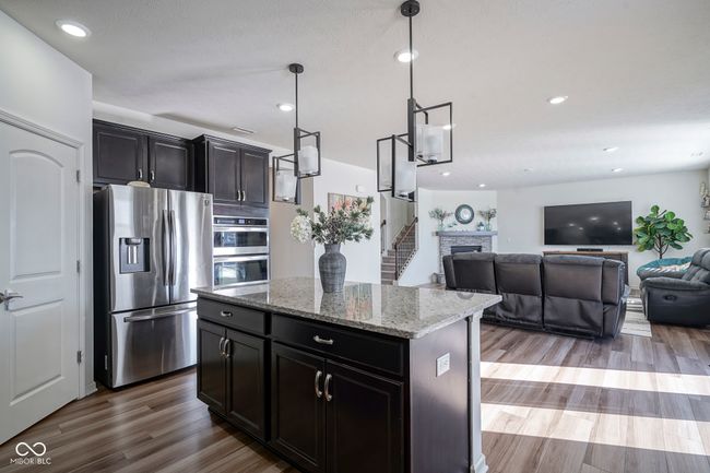 kitchen featuring light stone counters, wood finished floors, dark cabinetry, appliances with stainless steel finishes, and a center island | Image 21