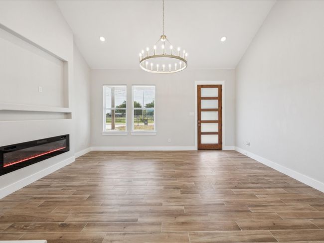Unfurnished living room featuring vaulted ceiling, a glass covered fireplace, a chandelier, wood finished floors, and recessed lighting | Image 8
