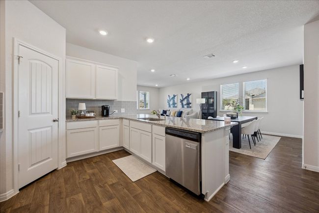 Kitchen featuring a peninsula, stainless steel dishwasher, dark wood finished floors, white cabinetry, and decorative backsplash | Image 19