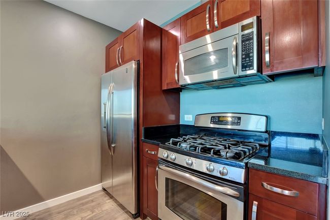 Kitchen featuring stainless steel appliances, dark stone counters, baseboards, light wood-style floors, and brown cabinetry | Image 9