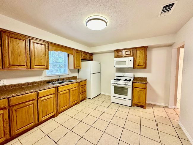 Kitchen featuring white appliances, brown cabinetry, dark countertops, and a textured ceiling | Image 6