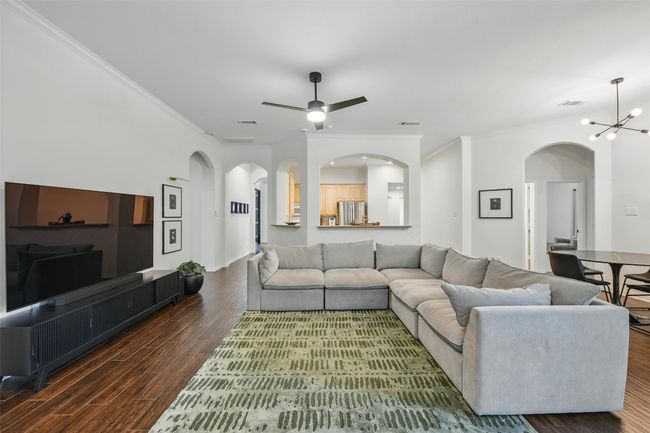 Living room with crown molding, wood finished floors, ceiling fan, arched walkways, and a chandelier | Image 15