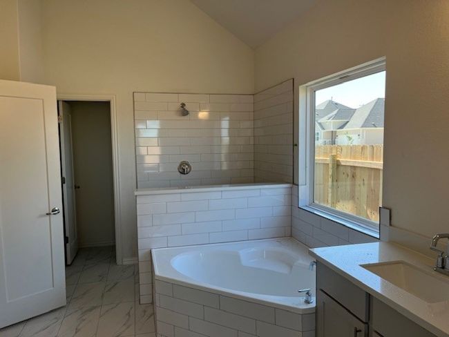 Full bath featuring a garden tub, marble finish floor, tiled shower, and vaulted ceiling | Image 7