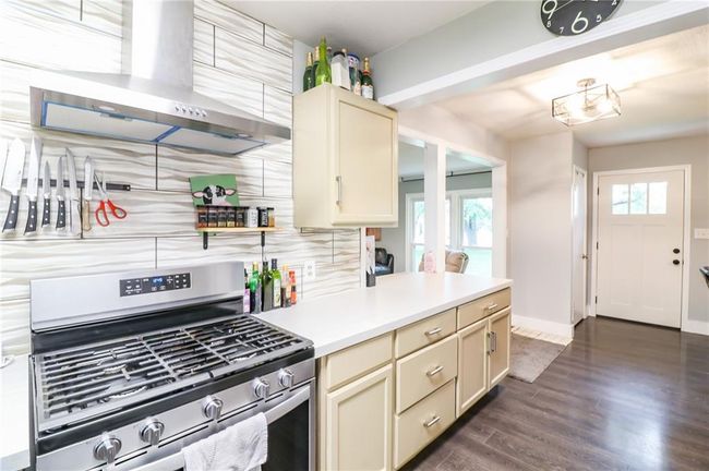 Kitchen with gas range, wall chimney exhaust hood, cream cabinetry, dark wood-style floors, and light countertops | Image 10