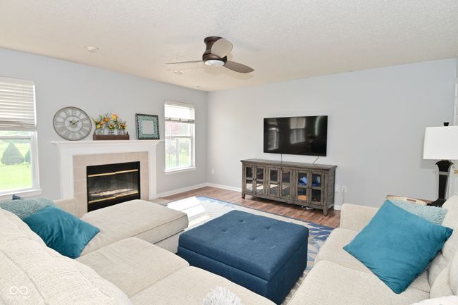 living area with a tiled fireplace, wood finished floors, ceiling fan, a textured ceiling, and baseboards | Image 7