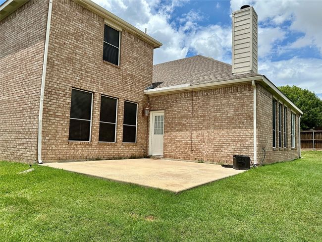Rear view of house with a patio area, a yard, a chimney, brick siding, and roof with shingles | Image 21