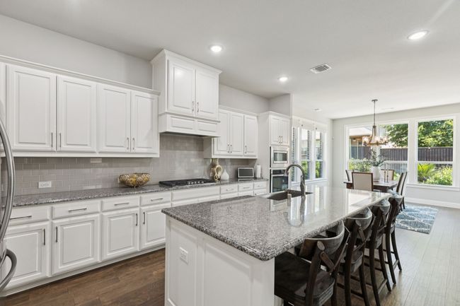 Kitchen featuring stainless steel appliances, dark wood-type flooring, a center island with sink, white cabinetry, and decorative backsplash | Image 12